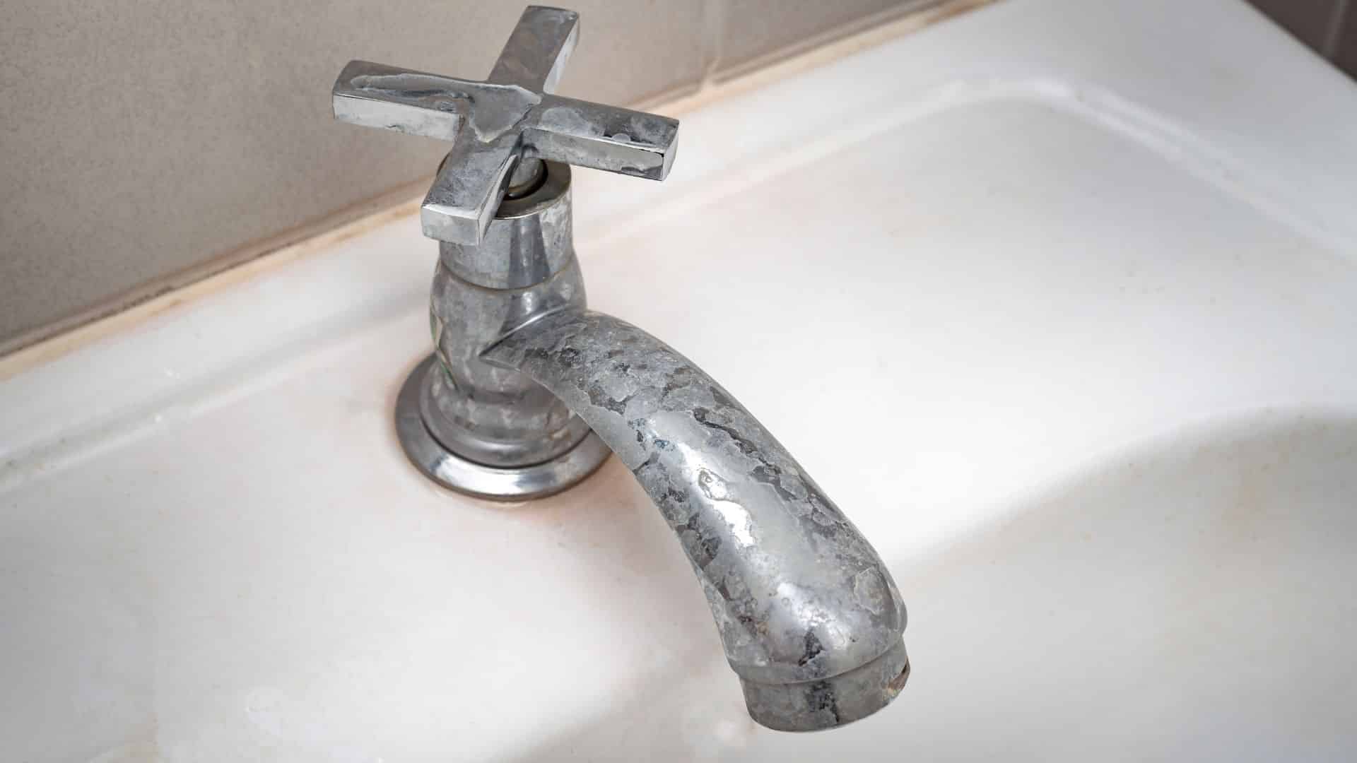 How to remove hard water stains from faucet showing mineral buildup on metal tap, highlighting limescale before cleaning treatment