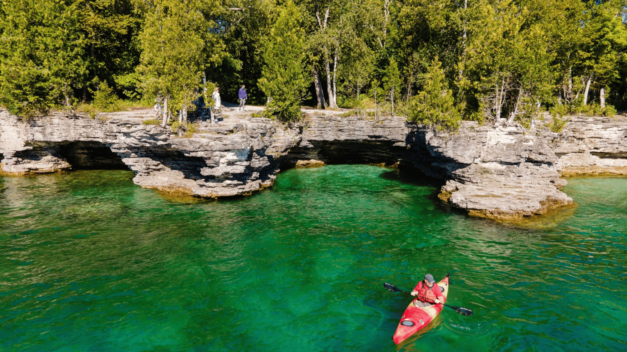 Kayaker on clear green water by limestone cliffs in Door County Wisconsin shoreline