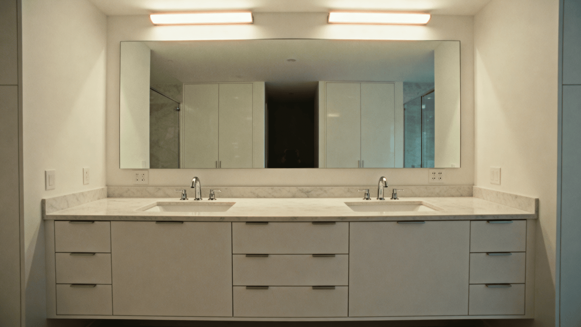 Minimalist bathroom with double vanity, large mirror, marble countertop, built-in storage, soft lighting, and clean neutral design style (1)