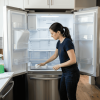 Person cleaning inside of an empty refrigerator in a bright modern kitchen