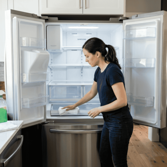 Person cleaning inside of an empty refrigerator in a bright modern kitchen