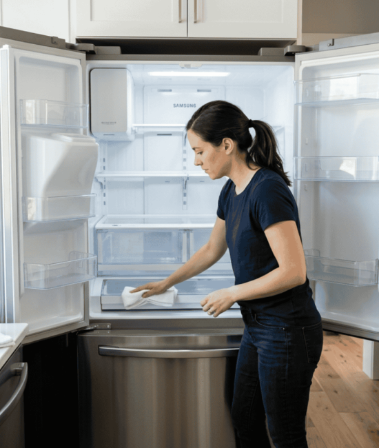 Person cleaning inside of an empty refrigerator in a bright modern kitchen