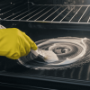 Person wearing gloves applying homemade cleaner inside oven with a brush.