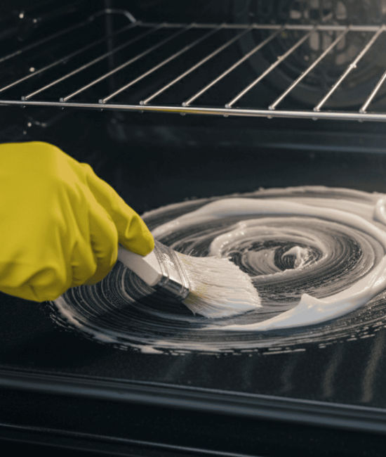 Person wearing gloves applying homemade cleaner inside oven with a brush.
