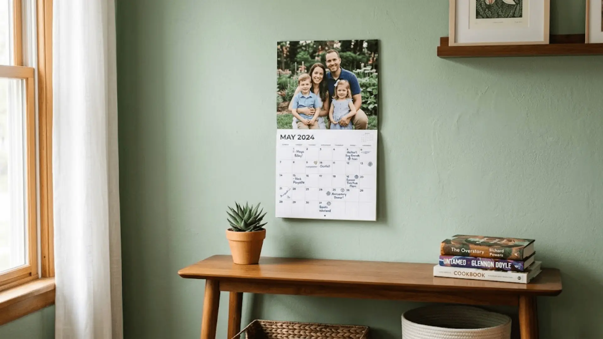 personalized photo calendar on sage green wall above wooden console with succulent and stacked books