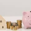 Piggy bank with stacked coins beside small house model, representing how to save for a down payment, building savings and planning for home purchase