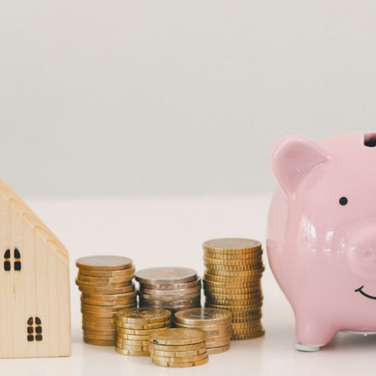 Piggy bank with stacked coins beside small house model, representing how to save for a down payment, building savings and planning for home purchase