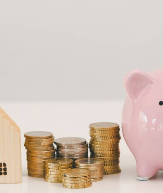 Piggy bank with stacked coins beside small house model, representing how to save for a down payment, building savings and planning for home purchase