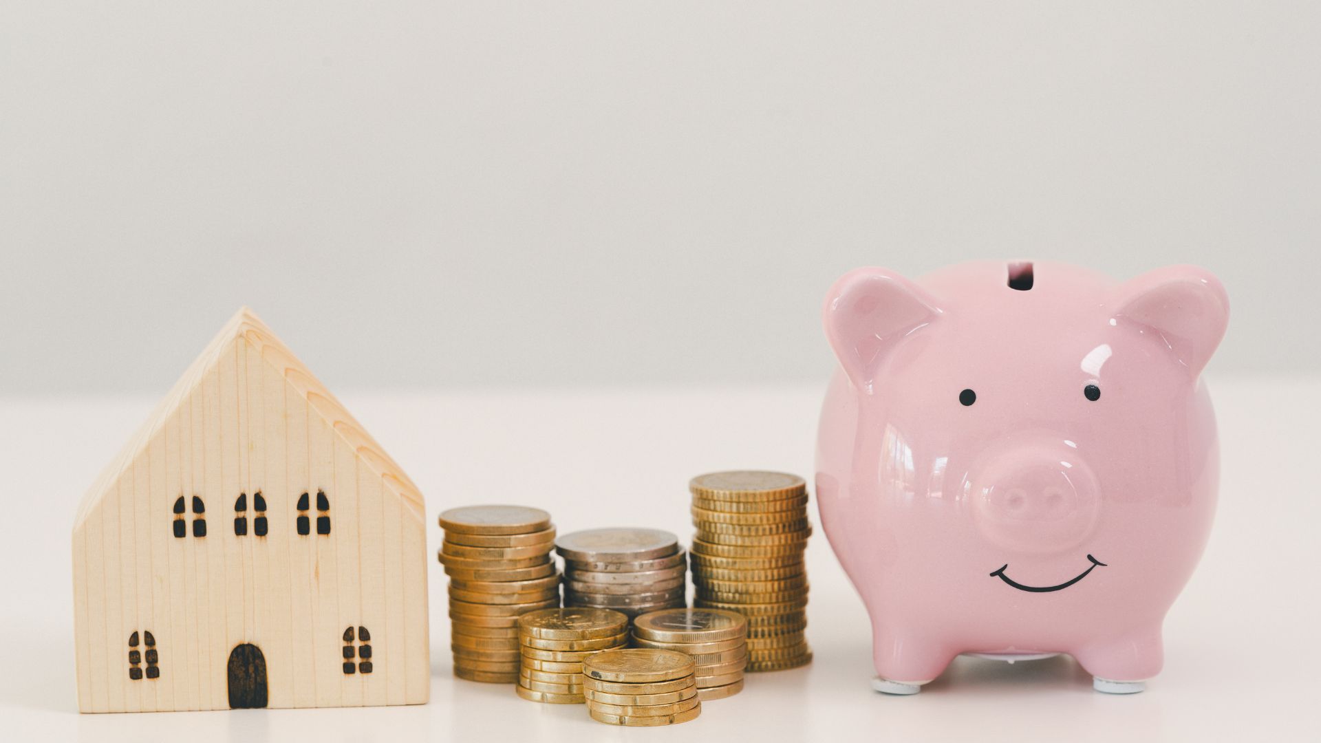 Piggy bank with stacked coins beside small house model, representing how to save for a down payment, building savings and planning for home purchase