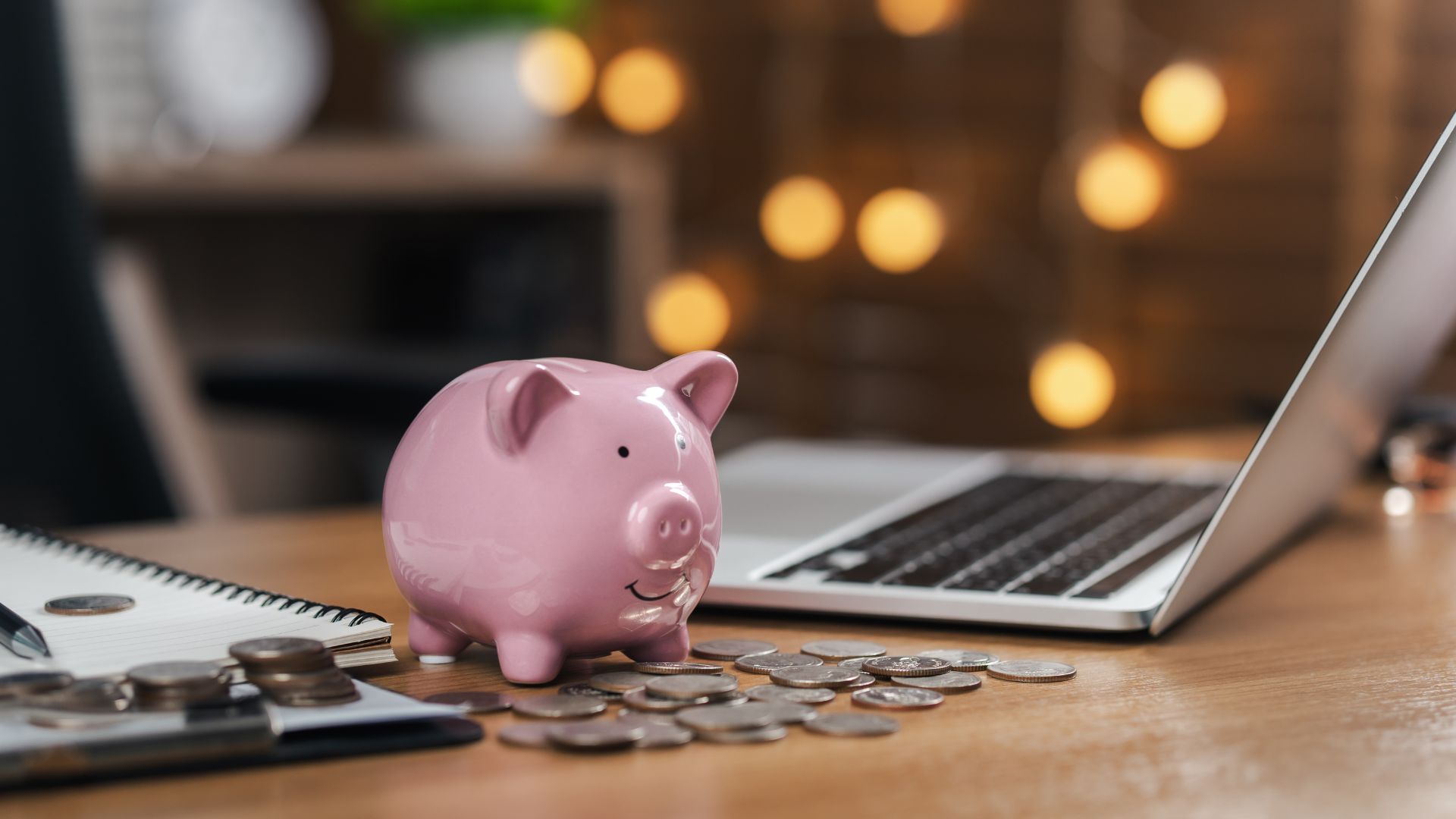 Pink piggy bank with coins beside a laptop and notebook, representing benefits of investing, saving money, financial growth, and smart wealth planning
