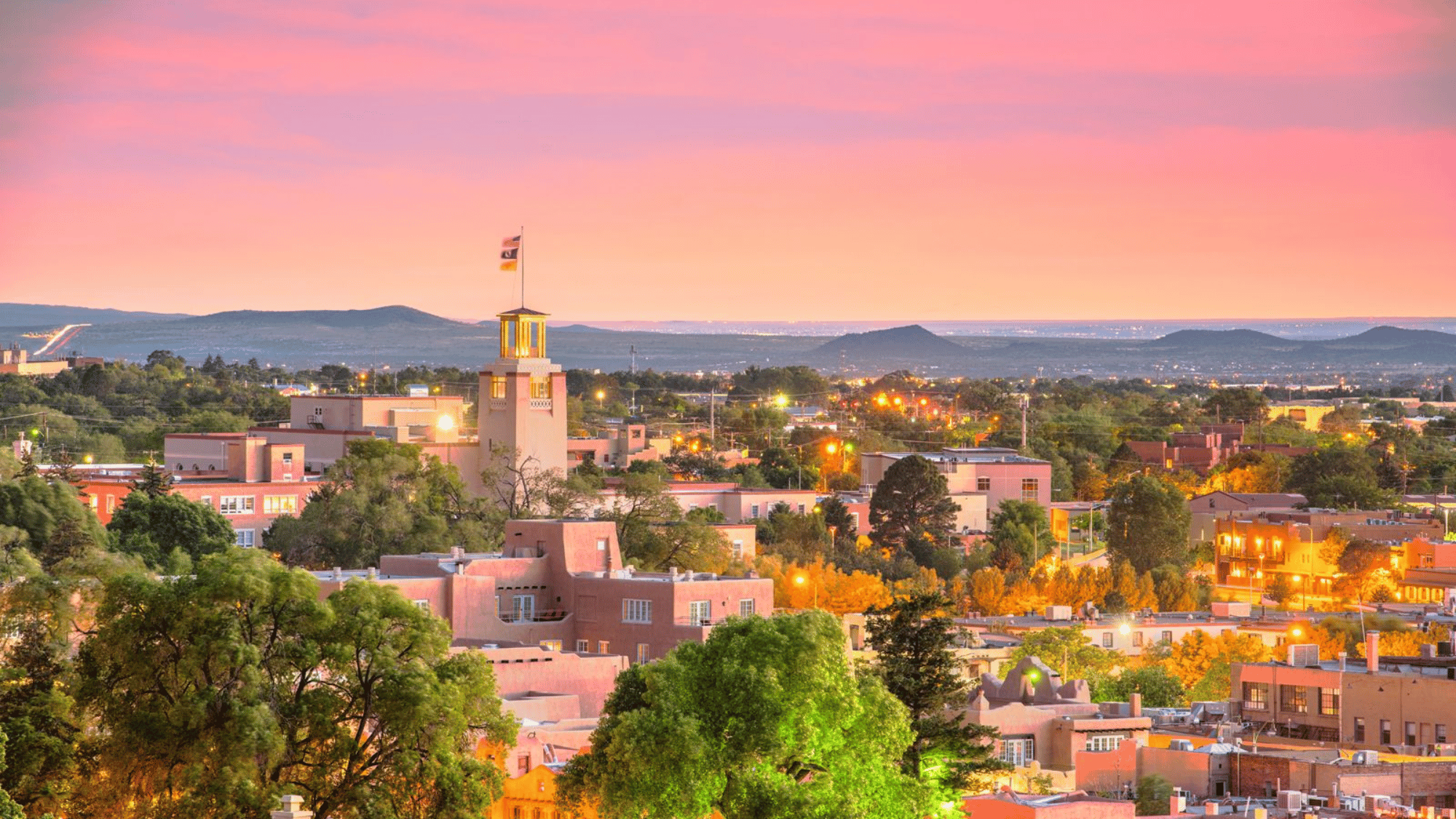 Santa Fe New Mexico skyline at sunset with adobe buildings and mountains in background.