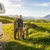 Family standing beside camper van on grassy hillside with mountain views in the background