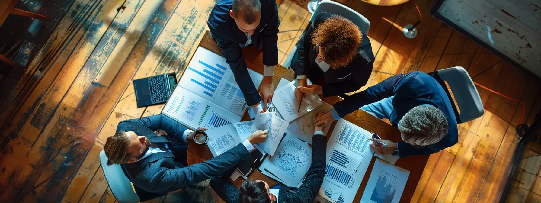Business team analyzing charts around wooden table in warmly lit office overhead view