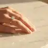 Hand with diamond engagement ring resting on marble table in soft natural light