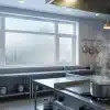 Stainless steel commercial kitchen with steam rising from pot on stove, hanging pans, large window