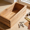 A finished wooden planter box with tools arranged on a workbench.