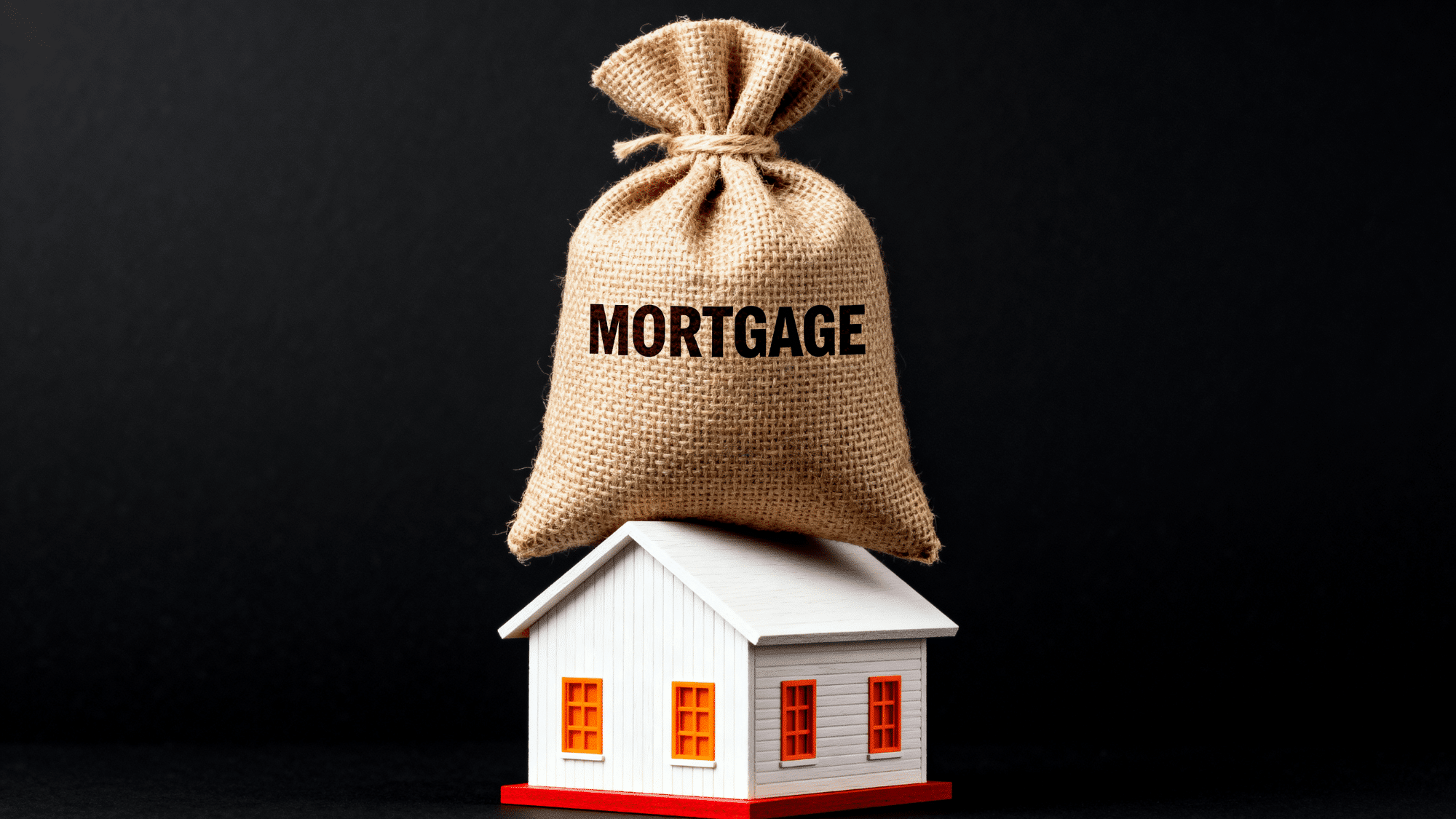Burlap sack labeled mortgage on house model symbolizing home loan burden and debt