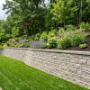 Concrete block retaining wall holding back soil on a sloped backyard with clean landscaping and level ground