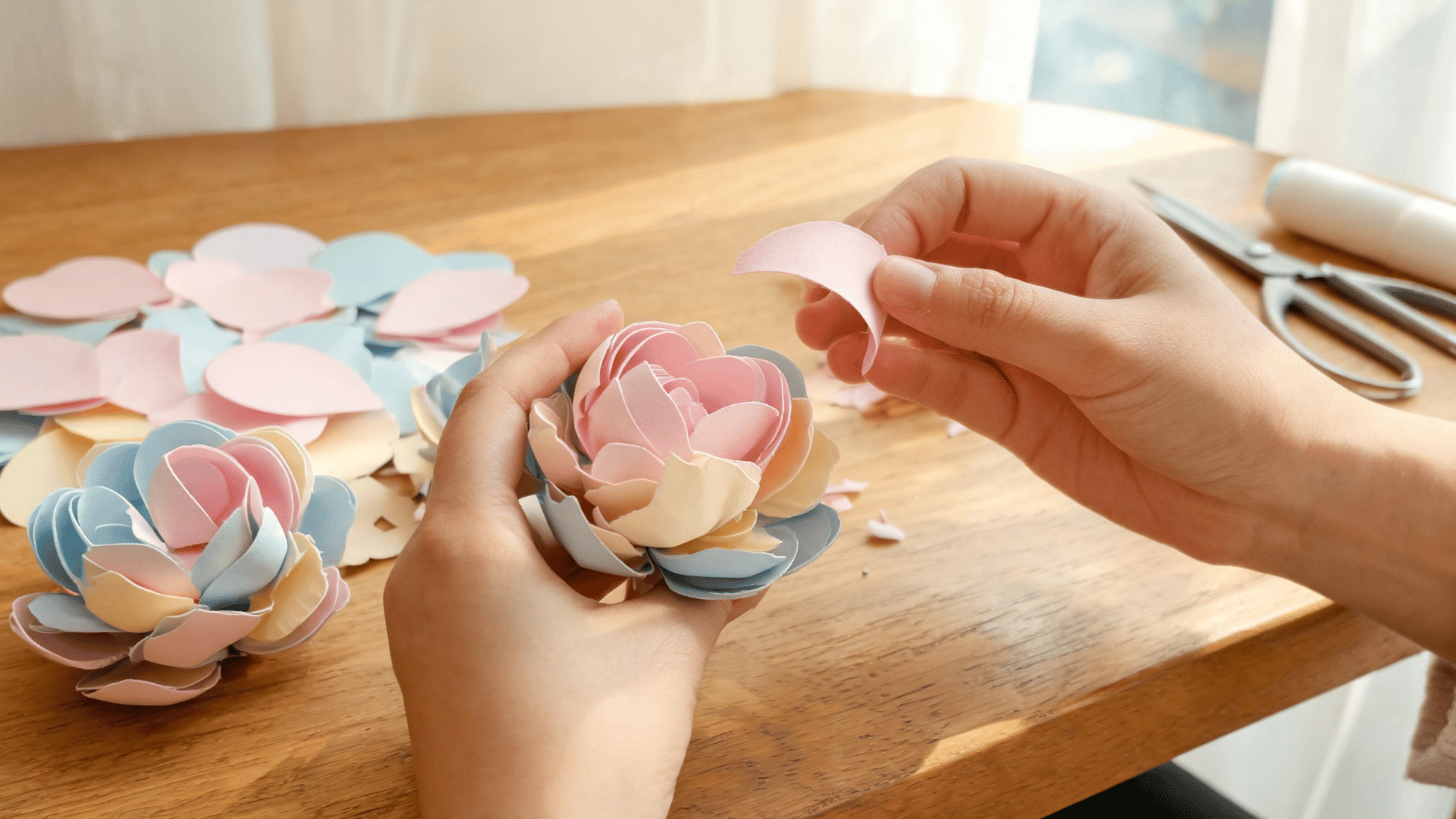 Hands folding colorful paper petals into flower blooms on a craft table. (1)