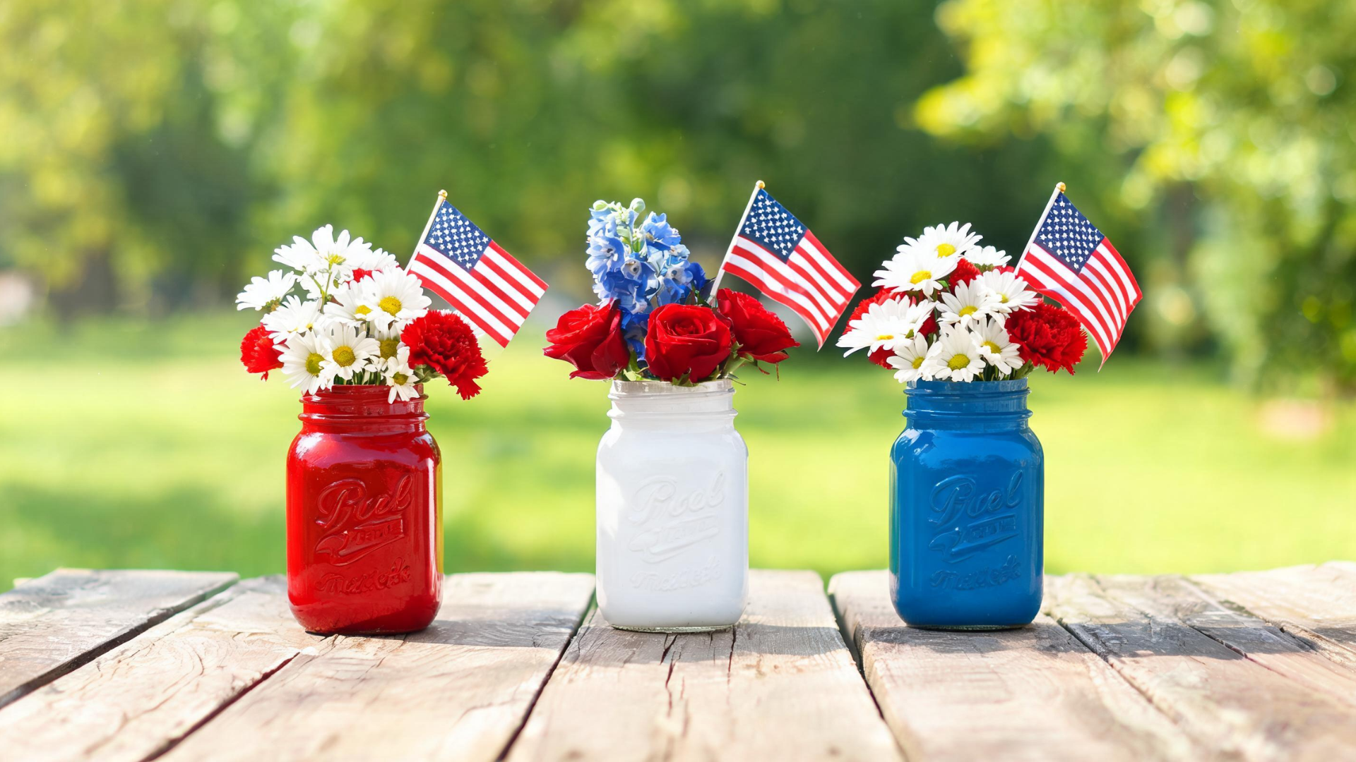 Mason jar centerpiece with red, white, and blue paint, small flags, and flowers on a Memorial Day table