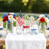 Memorial Day table with patriotic centerpieces, including flowers, candles, and flags in red, white, and blue theme