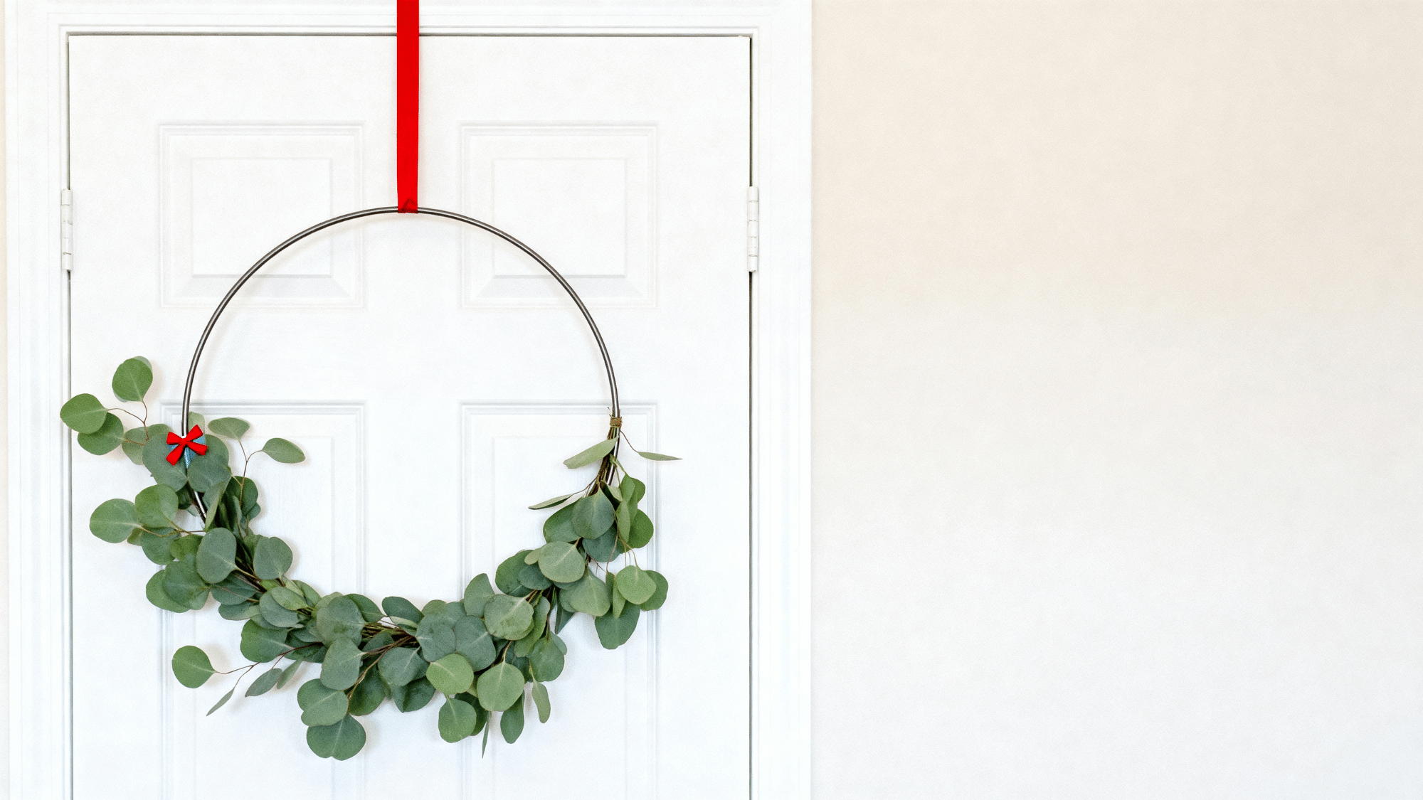 Minimal greenery hoop wreath with small red ribbon on modern door (1)