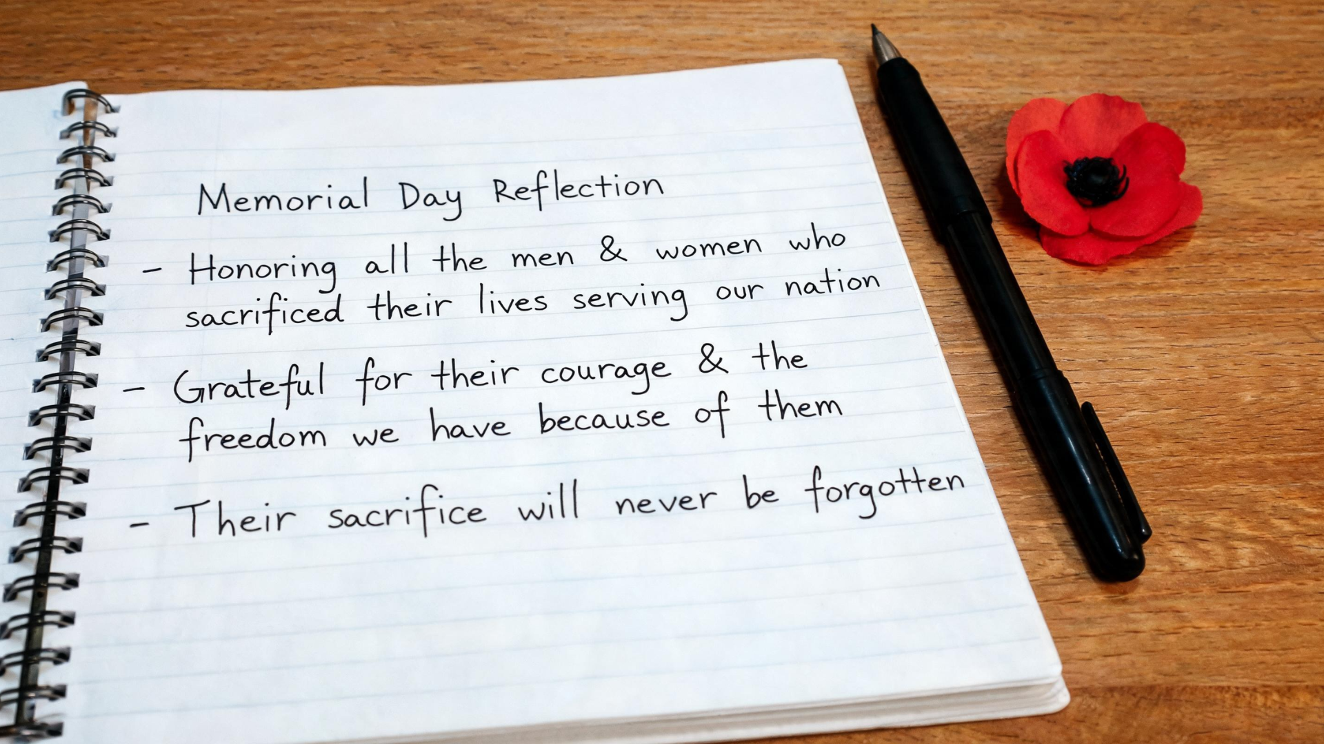 Notebook with a handwritten reflection about Memorial Day placed on a desk with a pen