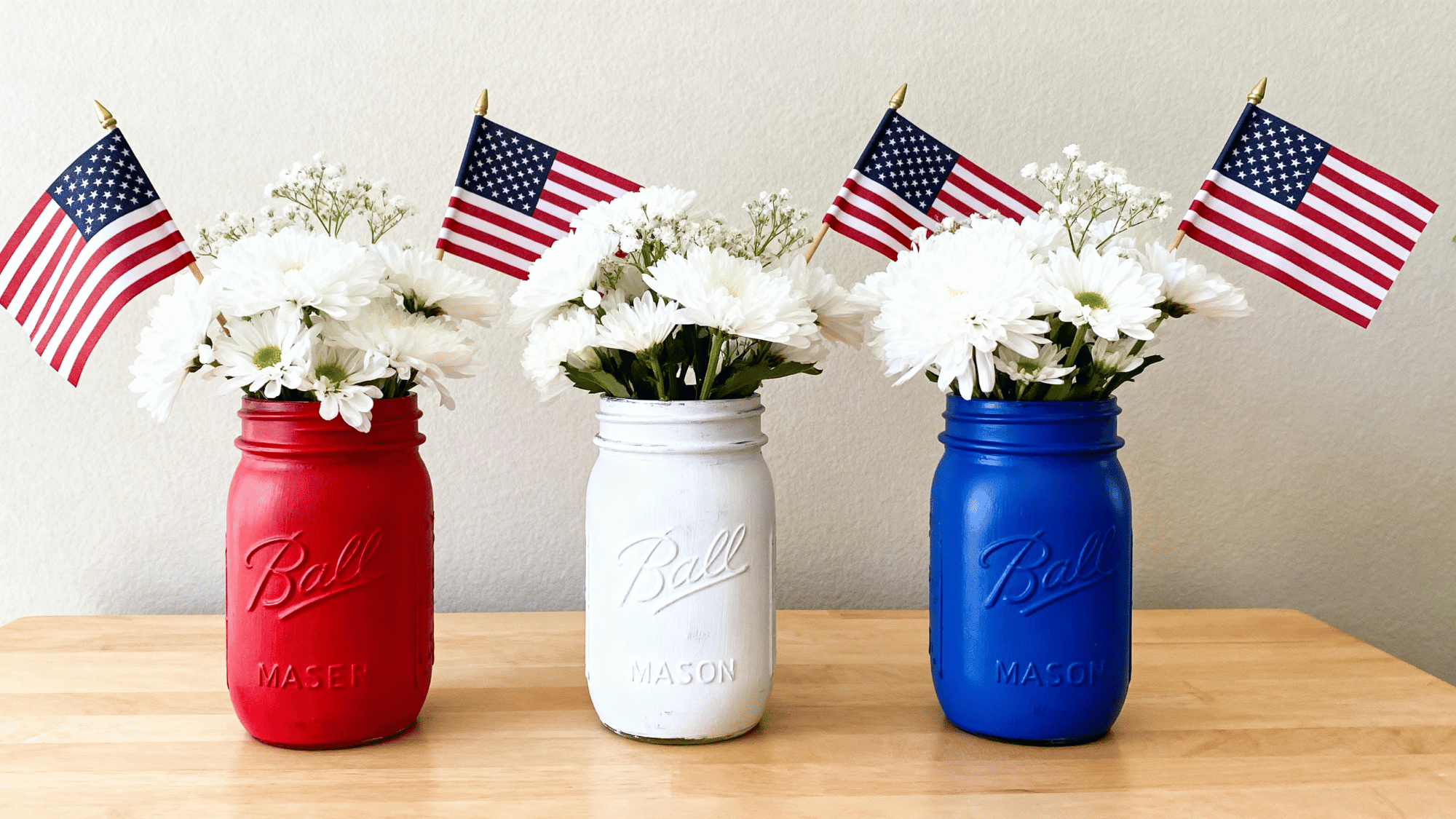 Painted mason jars with flowers and flags on a simple table.