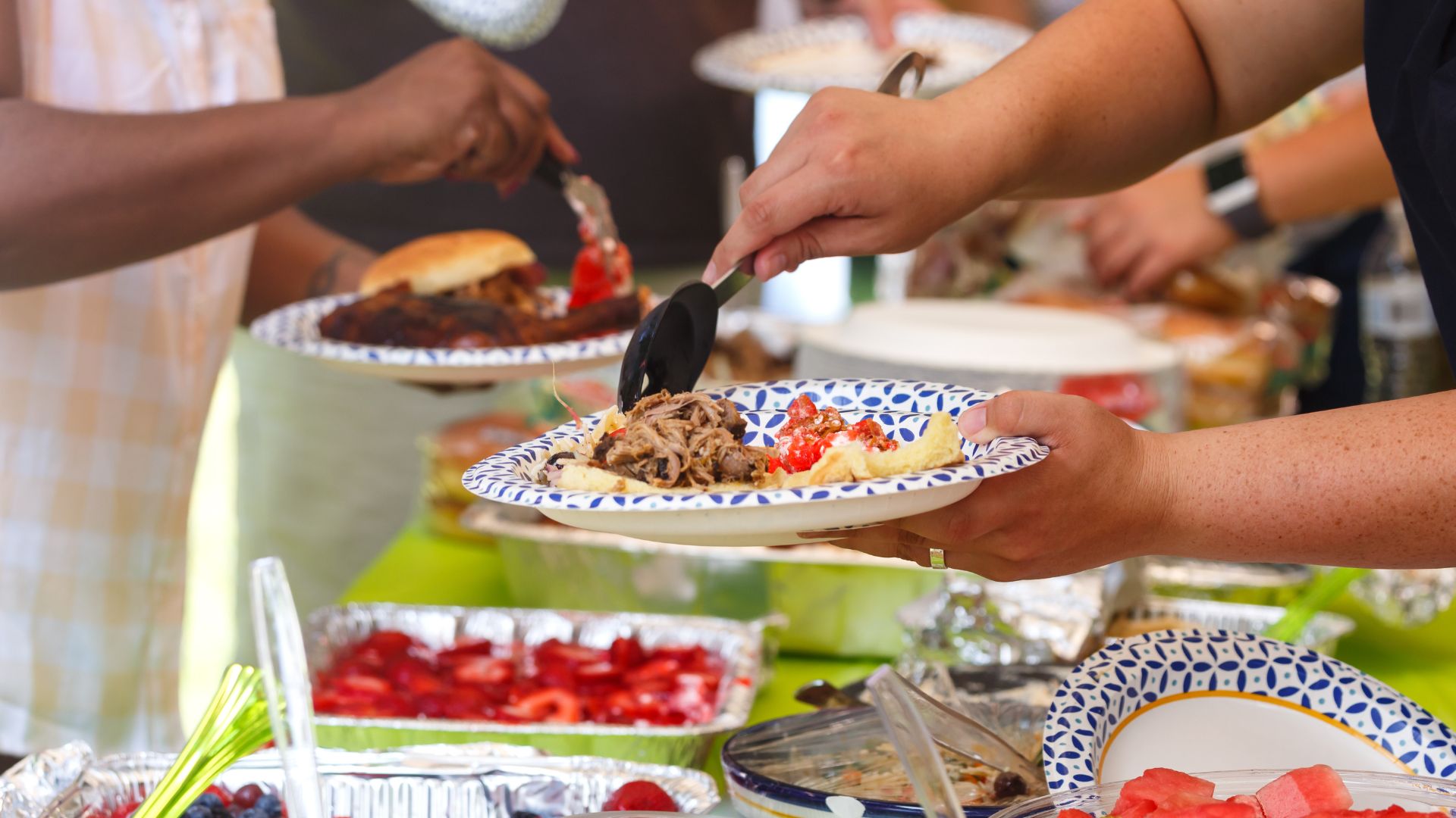 People serving food at a potluck buffet, a fun and social option among things to do on Memorial Day with friends, family, and shared meals