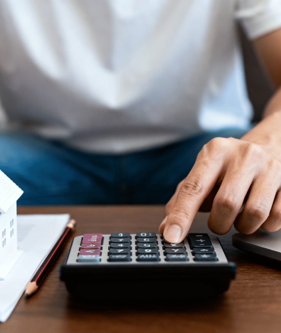 Person calculating mortgage payments with model house, calculator, and laptop on desk home.