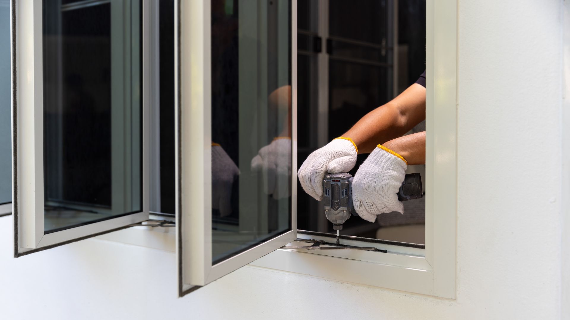 Person using a power drill to secure a window screen frame during the process of replacing the screen in a window