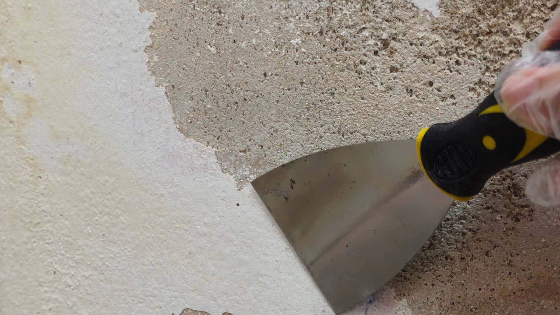 Person using a putty knife to remove old adhesive or grout as part of the preparation process for tiling a bathroom floor
