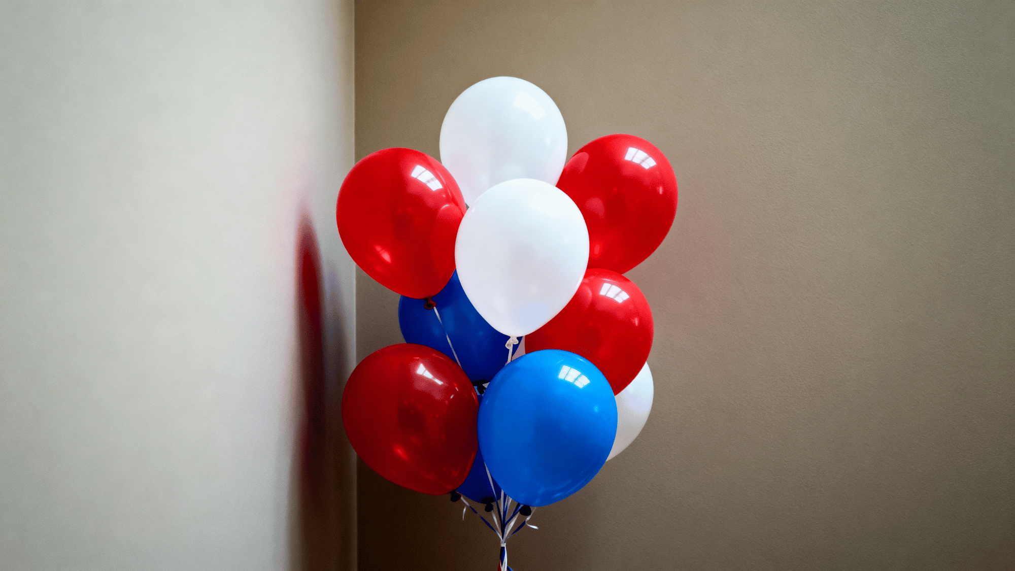 Red white blue balloon cluster against plain wall