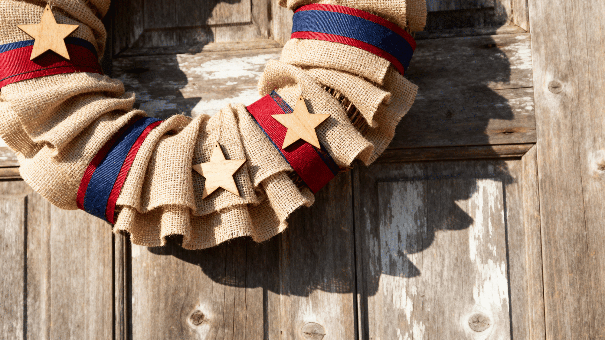 Rustic burlap wreath with patriotic ribbons and stars on wooden door