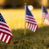 Small American flags placed in grass with sunlight and blurred flags in background.