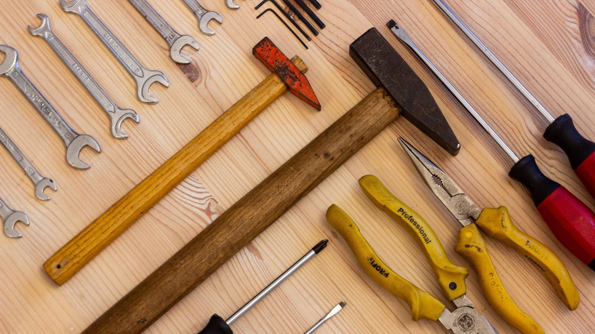 Tools for replacing a window screen, including wrenches, hammers, pliers, screwdrivers, and a rubber mallet, arranged on a wooden surface