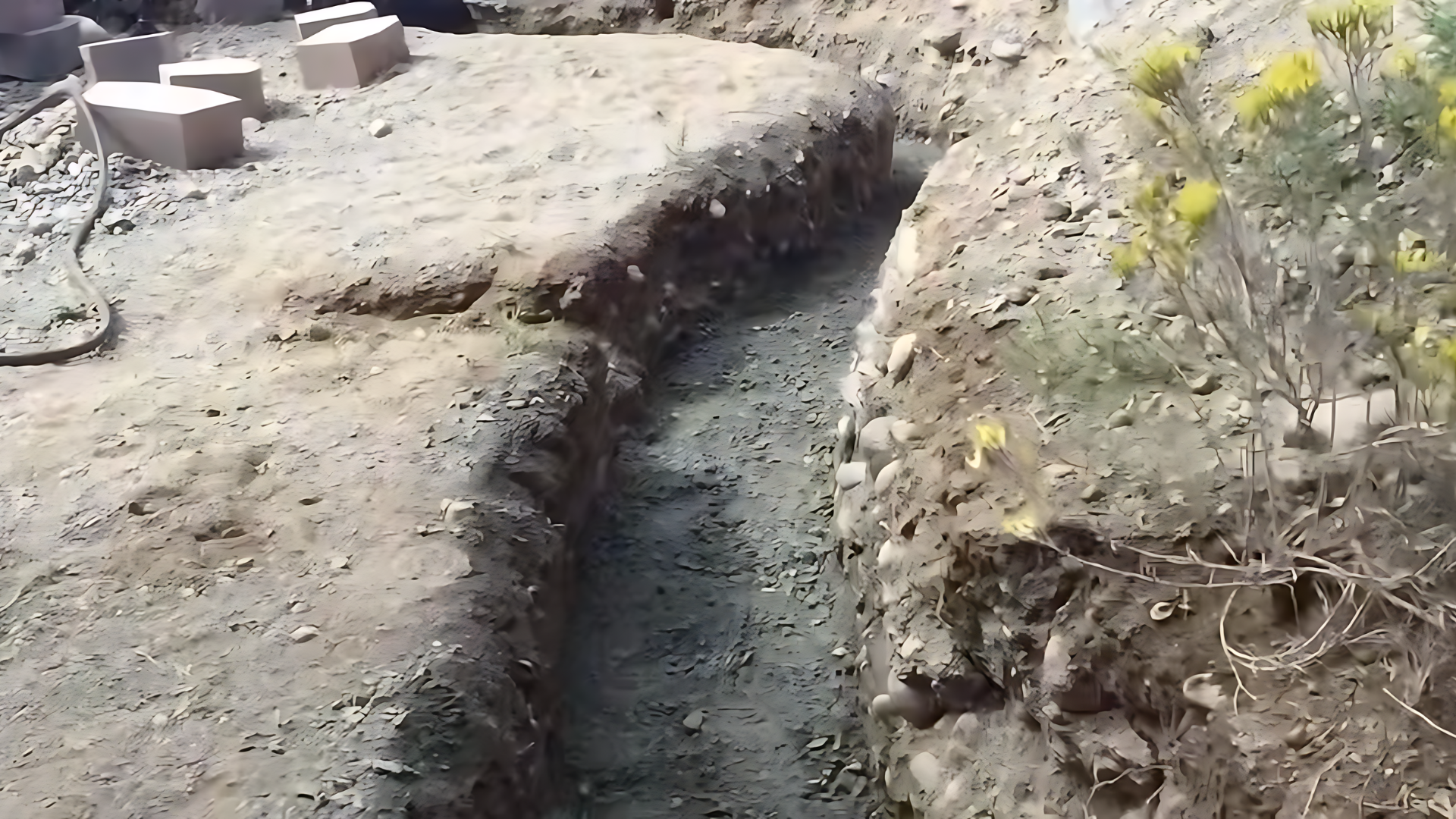 Wide trench dug in soil for retaining wall base, showing depth and width clearly, natural lighting