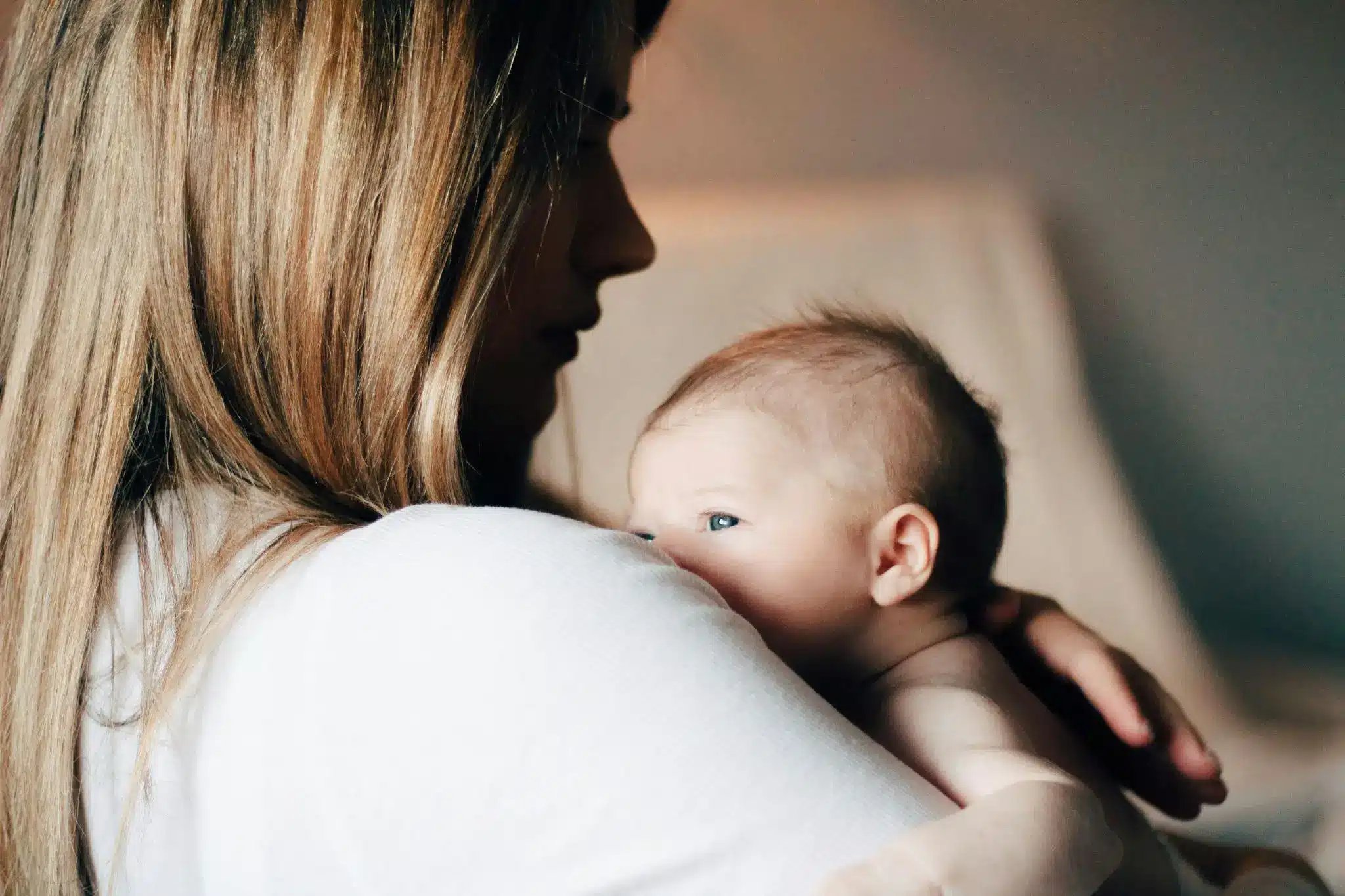 Woman holding newborn baby close in softly lit room