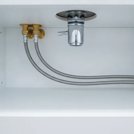 Under-sink plumbing with metal pipes and valves in a white cabinet