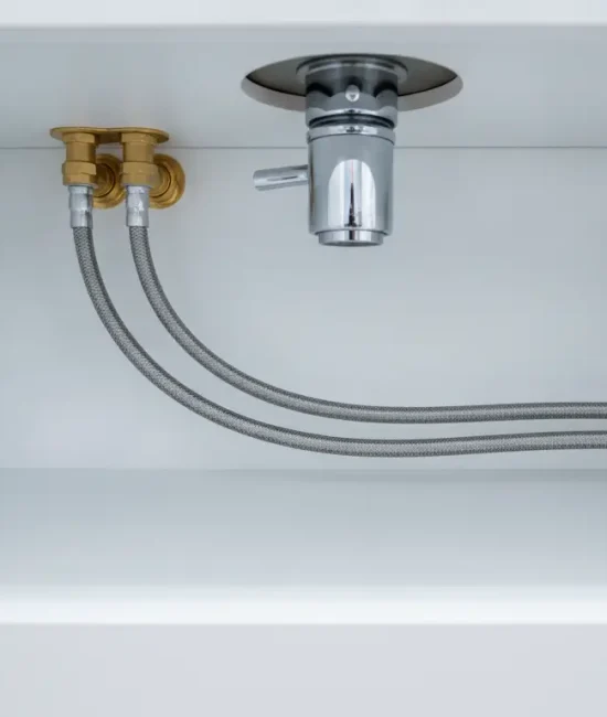 Under-sink plumbing with metal pipes and valves in a white cabinet