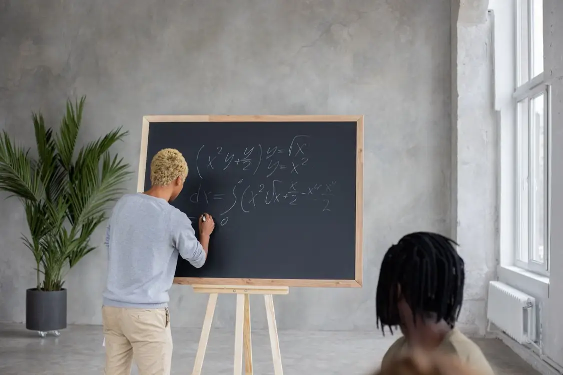 Person writing complex equations on a blackboard in a modern classroom setting