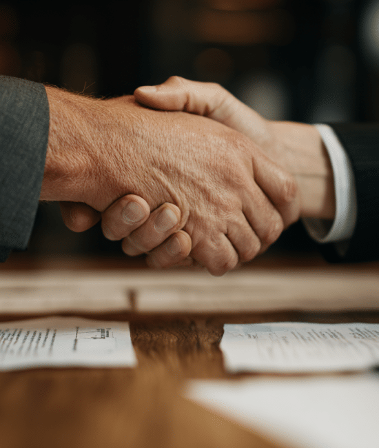 Two professionals in suits shake hands over a desk with signed documents, representing a family office services agreement.