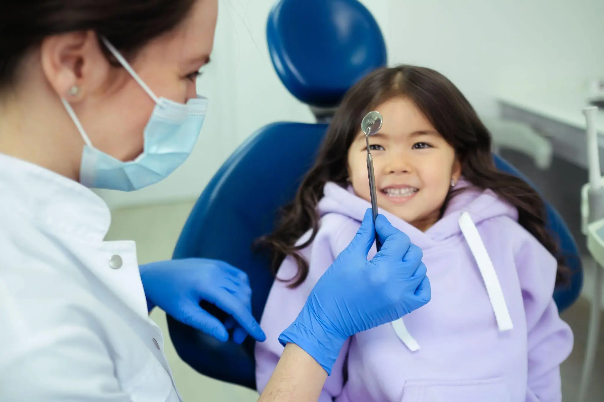 Dentist with child in dental chair holding a dental mirror in a clinic setting