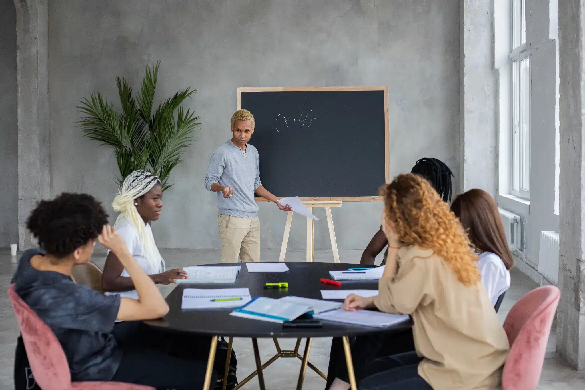 Group of people in meeting room with teacher at chalkboard teaching algebra equation
