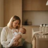Mother bottle-feeding baby in cozy kitchen with soft lighting and pacifiers on counter