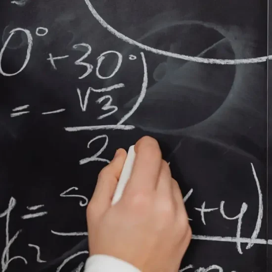 Hand writing mathematical equations with chalk on a blackboard in a classroom setting
