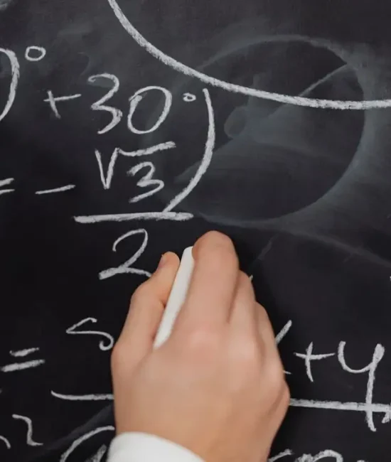 Hand writing mathematical equations with chalk on a blackboard in a classroom setting