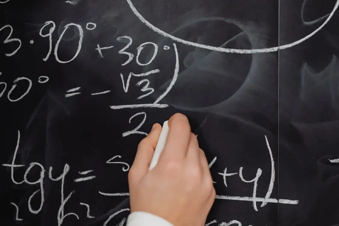 Hand writing mathematical equations with chalk on a blackboard in a classroom setting