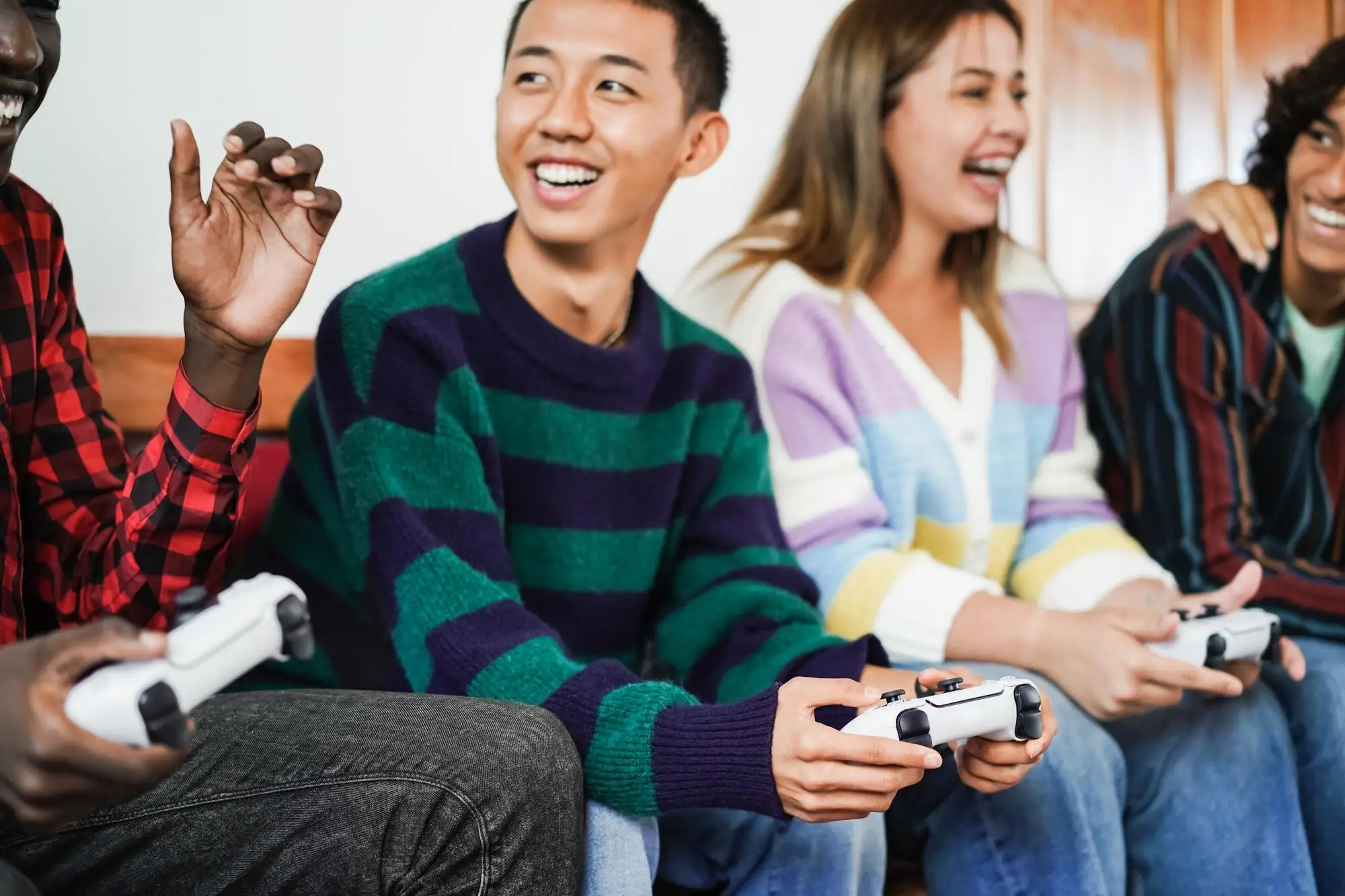 Group of friends playing video games on couch indoors with game controllers