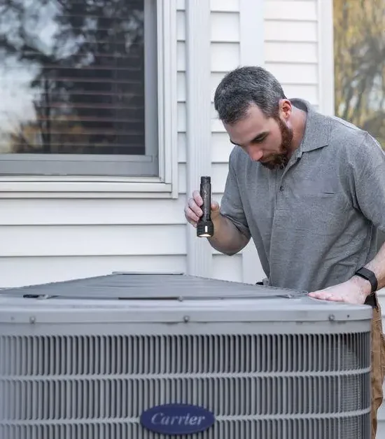Technician inspecting outdoor air conditioning unit beside house with flashlight